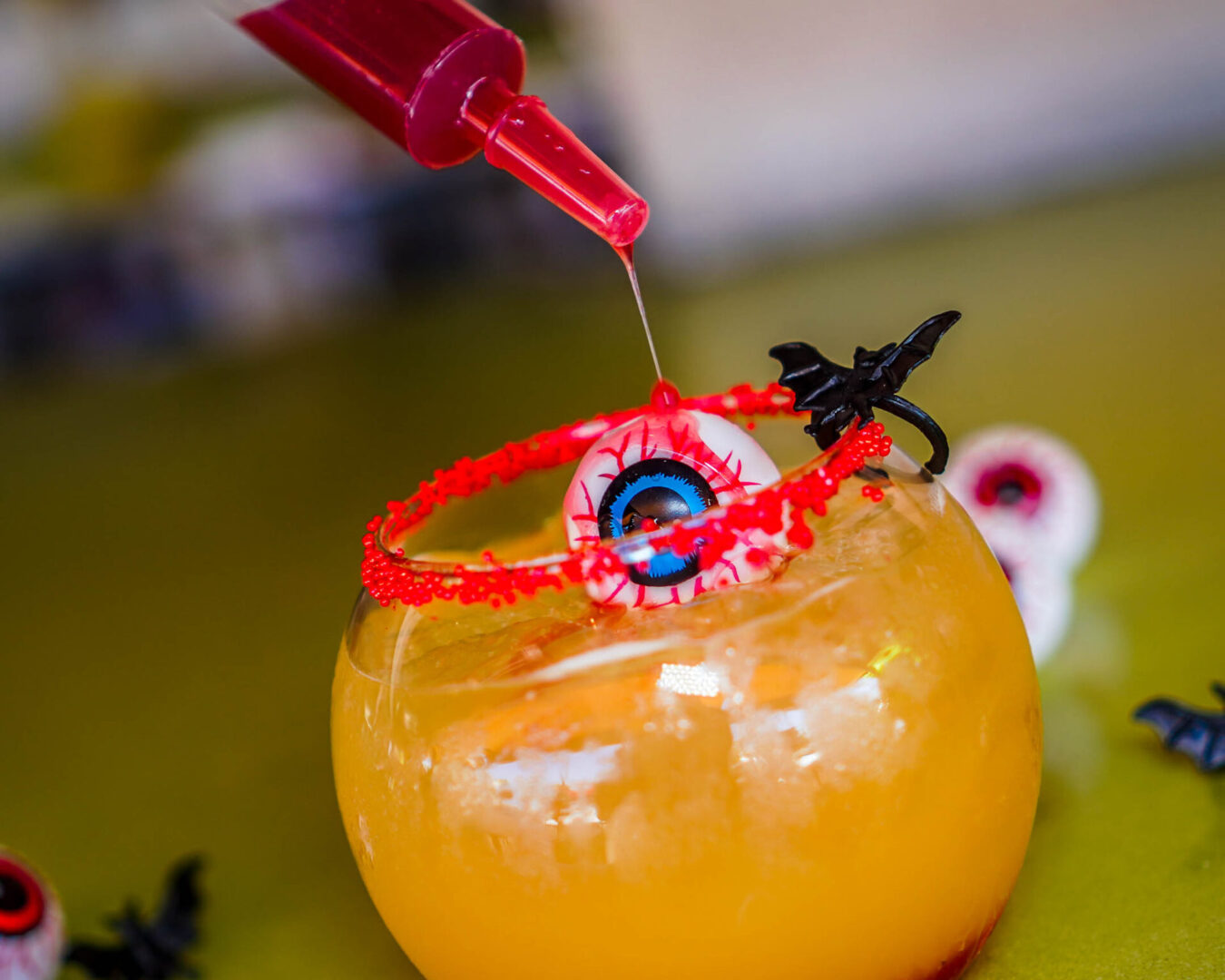 orange cocktail in round glass with syringe of red raspberry puree drizzling over drink.