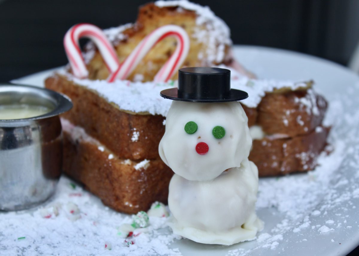 Cake Pop shaped like a snowman in a top hat sits beside Peppermint White Chocolate Stuffed French Toast.