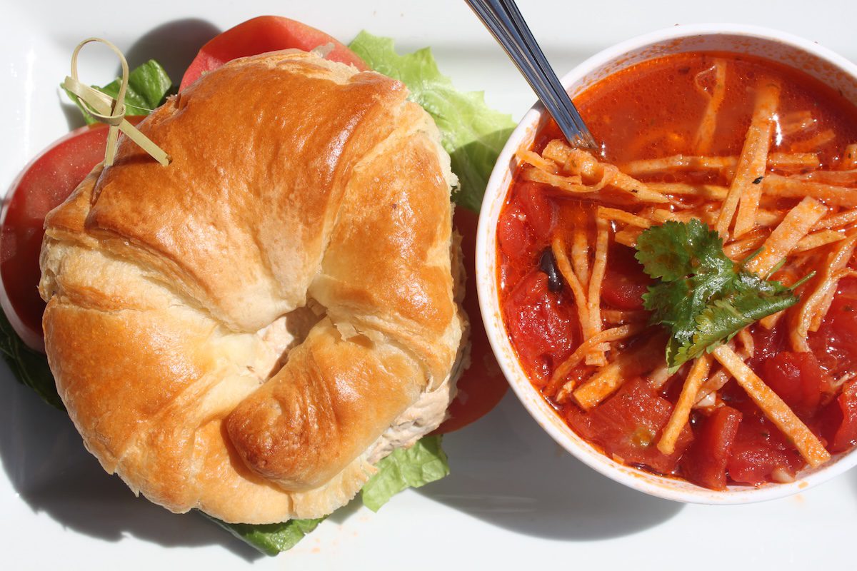 Overhead view of Chicken Salad Sandwich on a croissant beside a cup of Chicken Tortilla Soup.